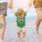 a toddler walking with his parents on a pier wearing a green OMG You're Home t-shirt featuring the original Chocolate Labrador Retriever dog design on the front